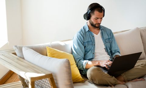 Young man sitting on couch at home with headphones and laptop