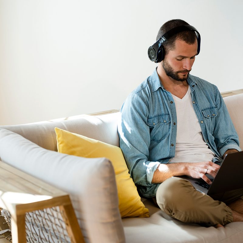 Young man sitting on couch at home with headphones and laptop