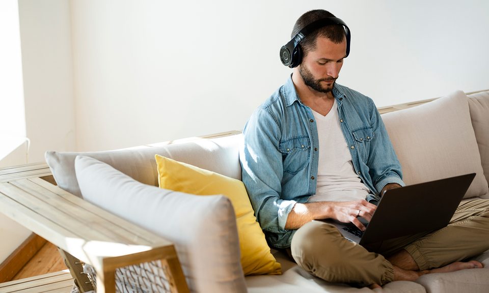 Young man sitting on couch at home with headphones and laptop