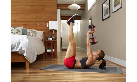 A woman in her bedroom performing dumbbell exercises with the Bowflex SelectTech adjustable dumbbells.