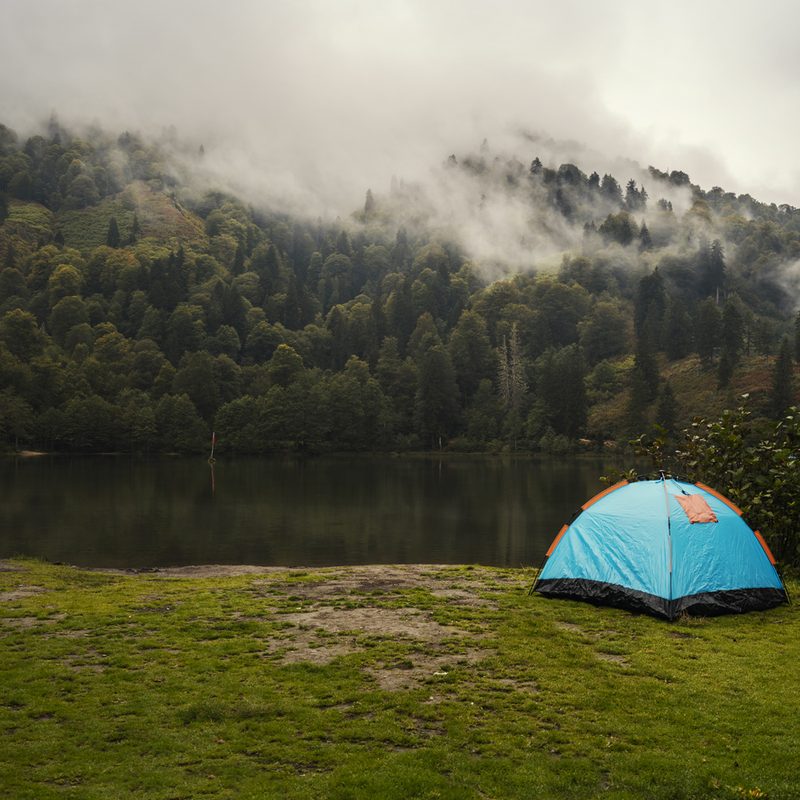 A blue camping tent near a lake.