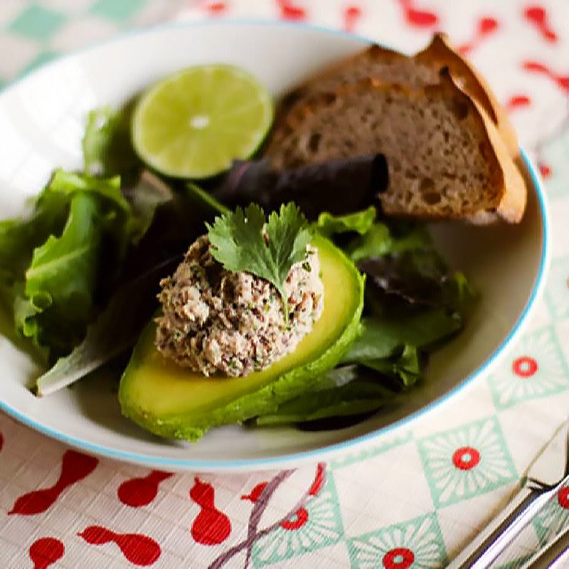 A bowl of cilantro-lime sardine salad in avocado halves and utensils on a table mat.