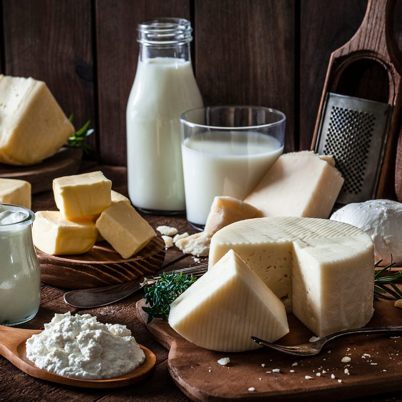 Milk, yogurt, butter, cheeses, and eggs shot on rustic wooden table.