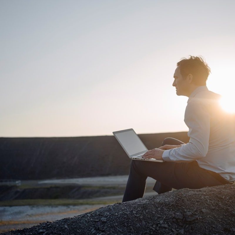 A man with a laptop under the sunset.