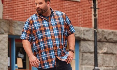 A man wearing jeans and polo for big frames outside a storefront with a streetlight.