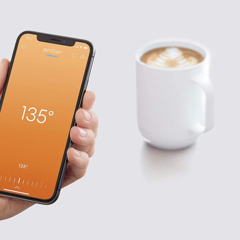 A hand holding a phone, with a cup of coffee near it.