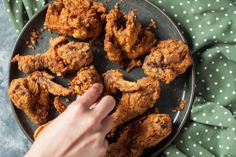 A hand reaching for a piece of crunchy buttermilk fried chicken.