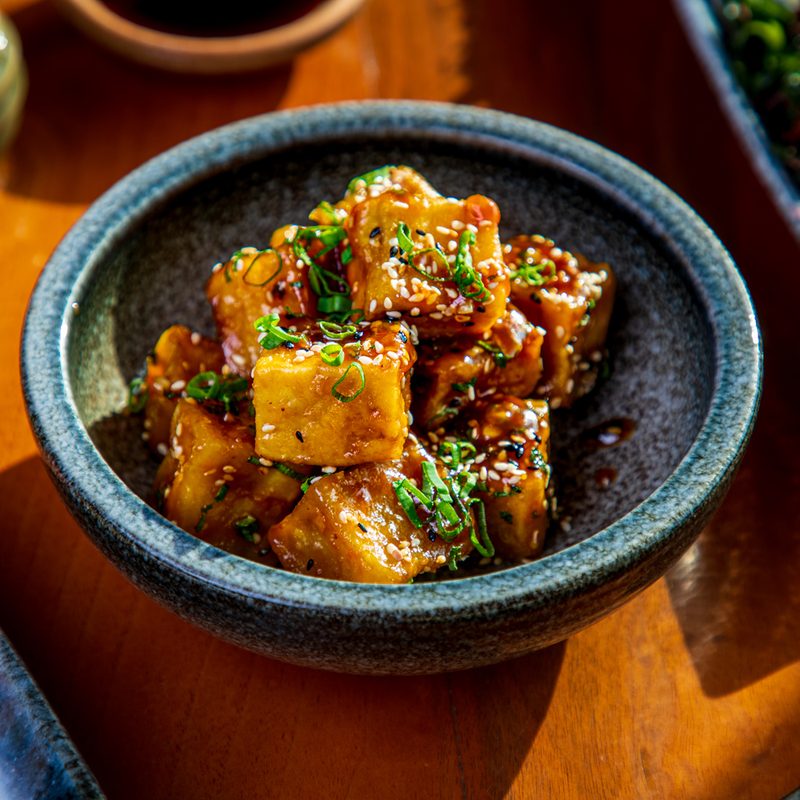 Tofu cubes with black and white sesame and chopped scallion served in a bowl on a table.