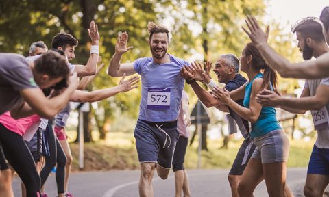Young happy man greeting with group of supporters at finish line after marathon race.