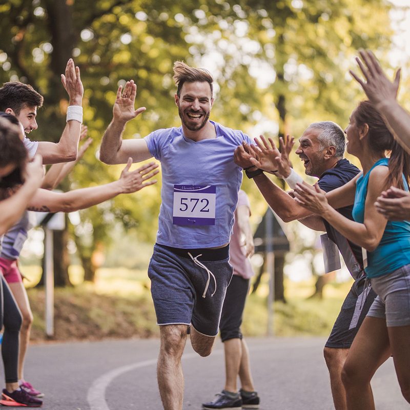Young happy man greeting with group of supporters at finish line after marathon race.