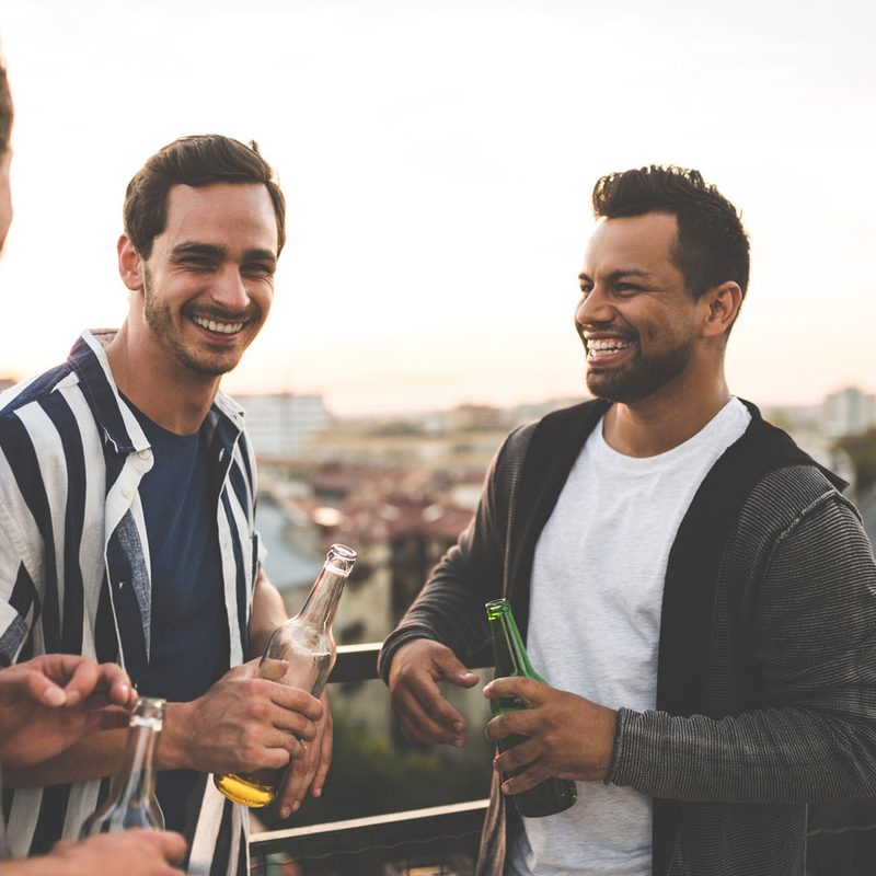 Three men holding bottles of beer at a terrace.