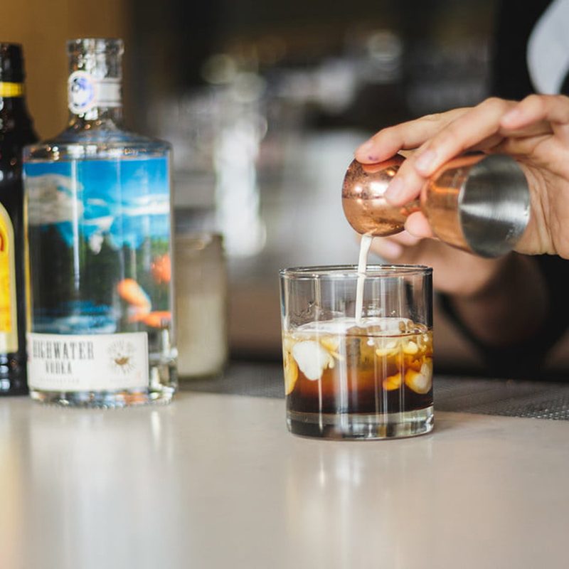 Pouring half and half in White Russian cocktail at bar.