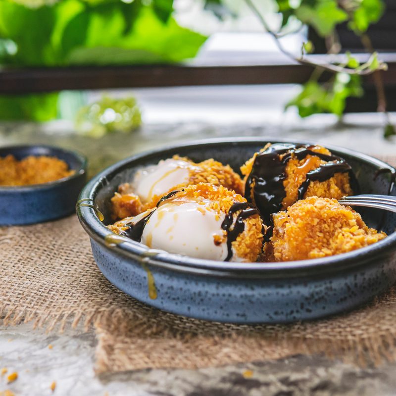 Fried white ice cream on blue plate, grey table with flowers near window.