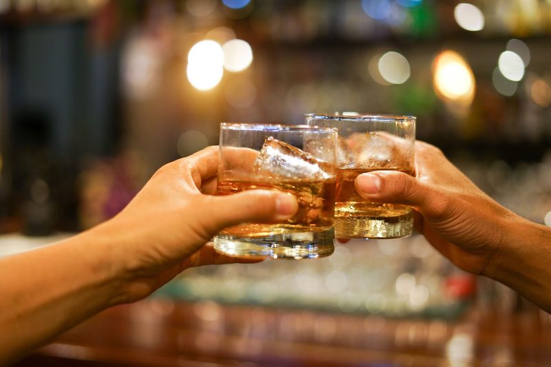 Two men in a bar clinking glasses of beer.