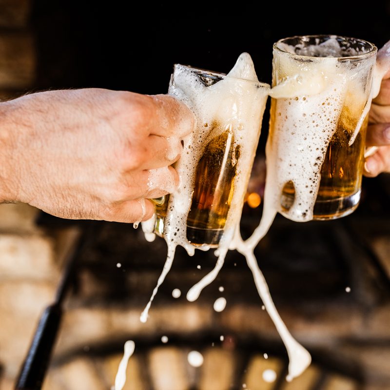 Two men spilling their glasses of beer while toasting with them.