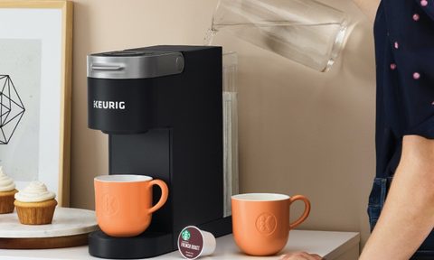 Keurig K-Slim Coffee Maker being filled with water and mugs nearby.