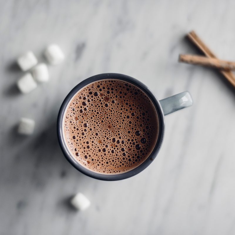 A cup of hot chocolate with marshmallows and cinnamon on a table.