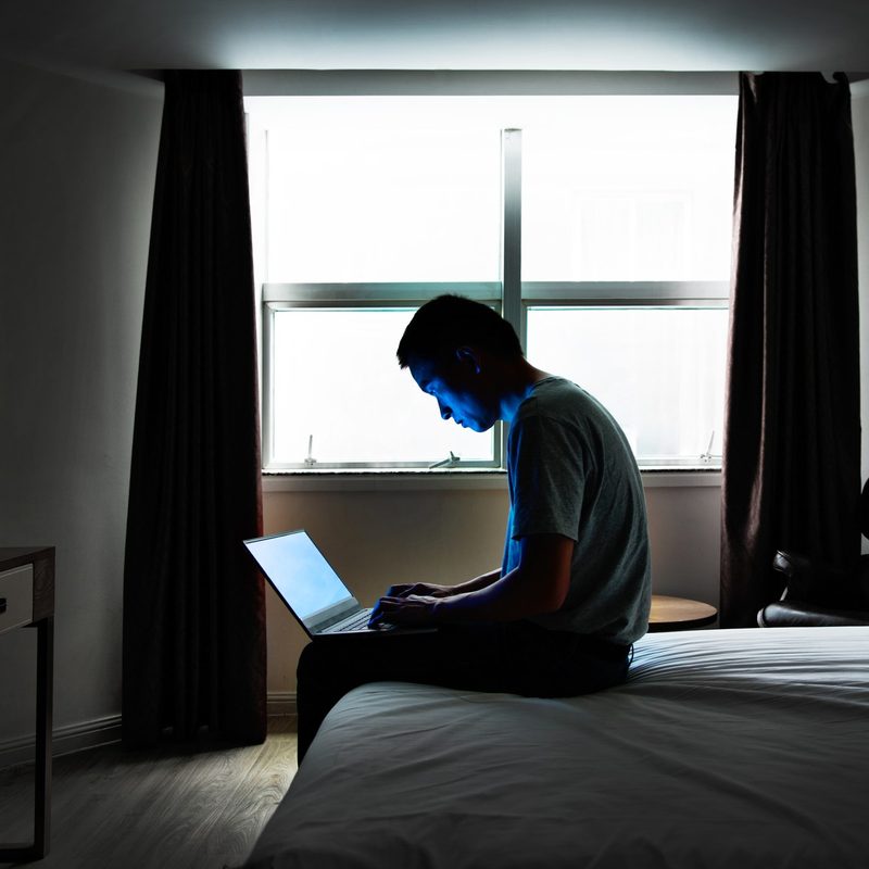 A man sitting in his hotel room alone with his laptop.