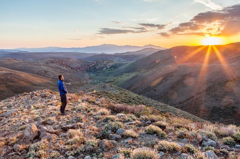 A person standing on a hill alone at sunset