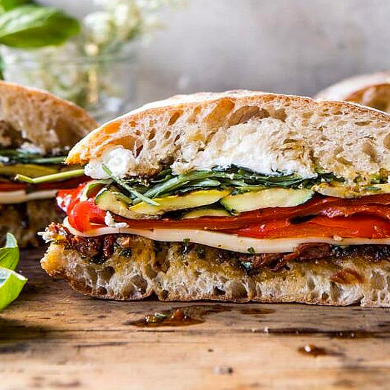 Three loaves of marinated veggie cheese sandwiches with sun-dried tomato pesto on a wooden surface.