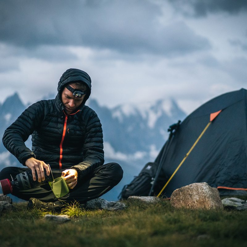 A man preparing a hot beverage beside his tent on a mountain.