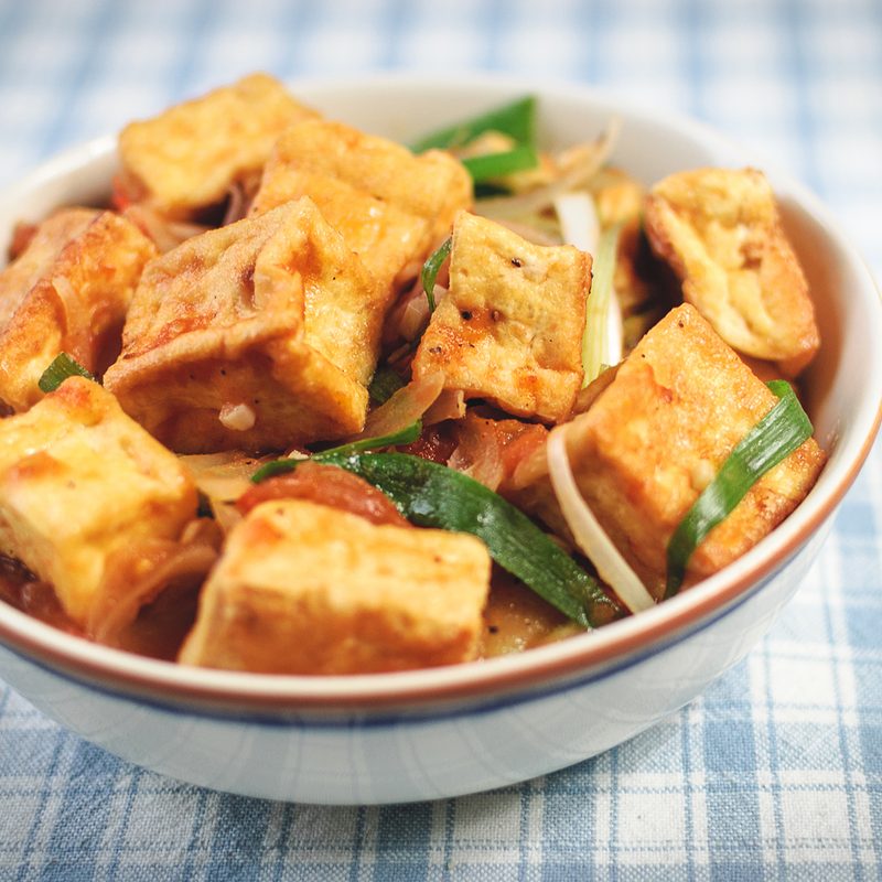 Cubes of tofu served in a bowl on a blue checkered table cloth.