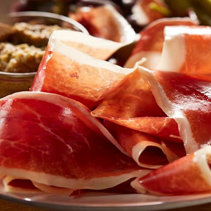A close-up of a plate of sliced Jamon Ibérico de Bellota and other food assortments.