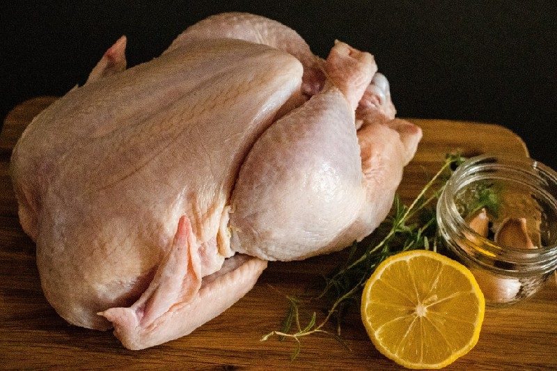 Raw chicken with lemon and other spices on a cutting board.