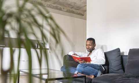 A man reading a book on a couch in the living room.