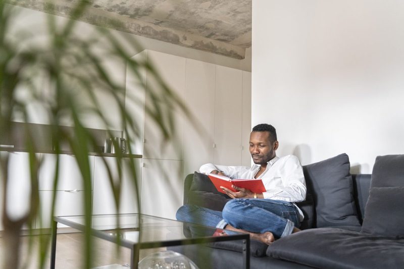 A man reading a book on a couch in the living room.