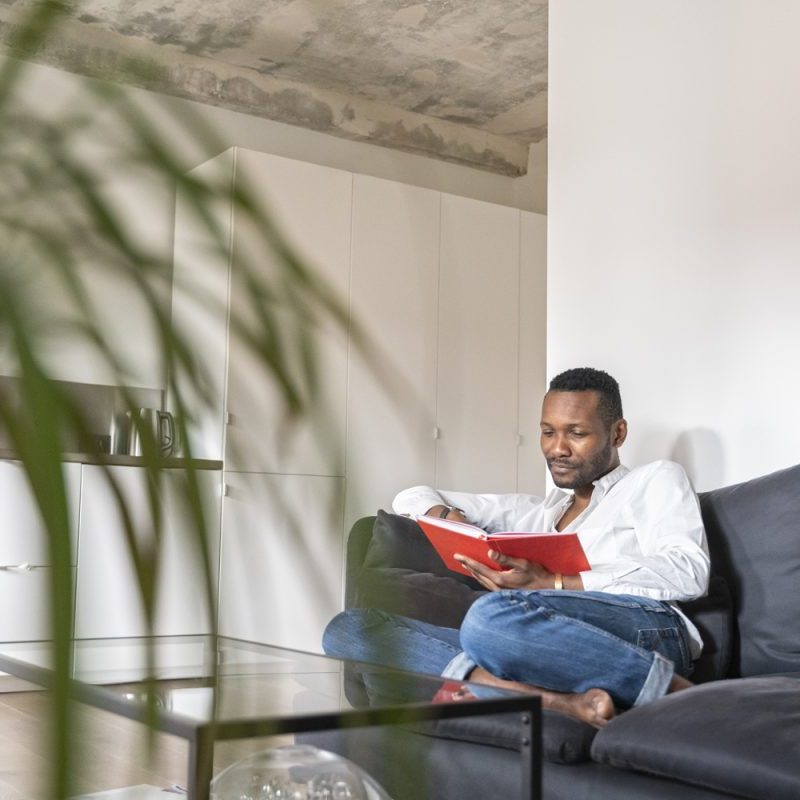 A man reading a book on a couch in the living room.