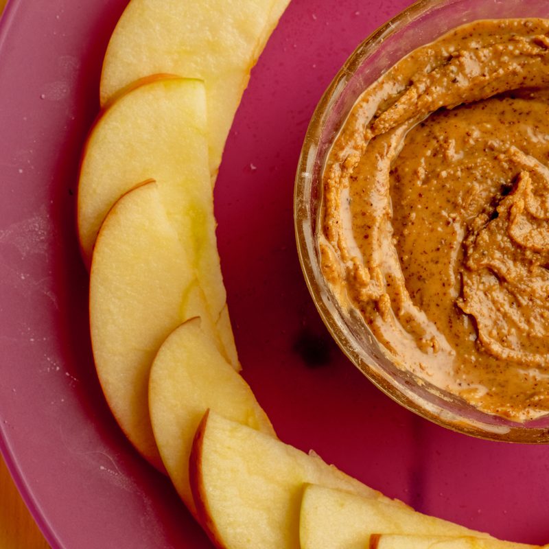 Sliced apples and almond butter served on red plate.