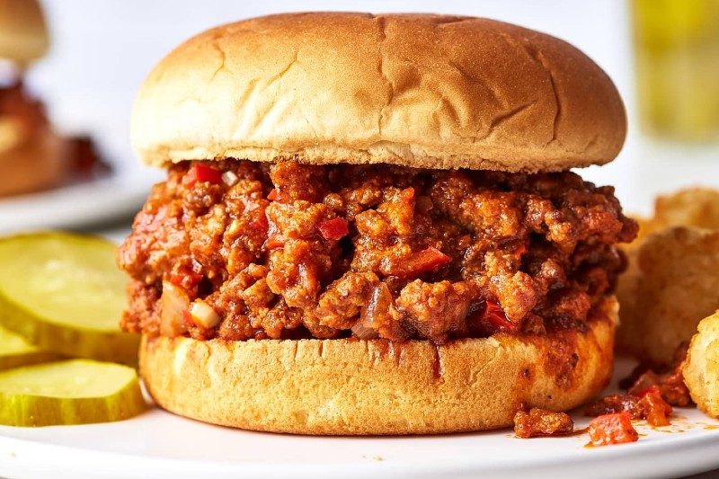 A sloppy joe sandwich on a plate with pickles.
