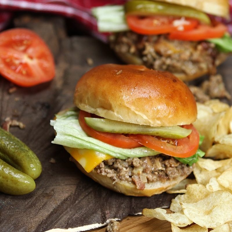 A sloppy joe with pickle and chips.