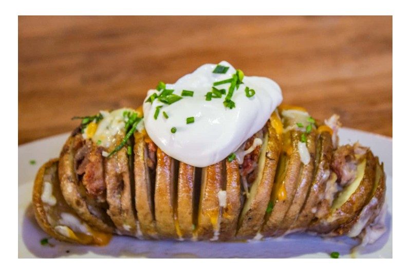 A smoked Hasselback potato topped with sour cream and chives.