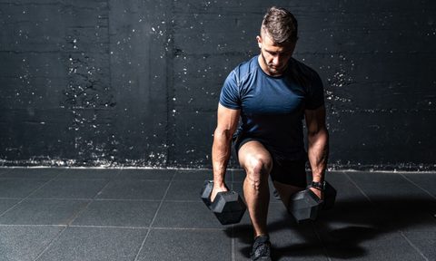 A man uses two dumbbells to perform a split squat.