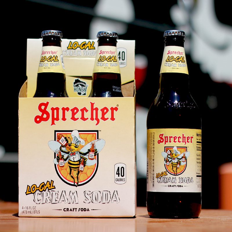 A pack of Sprecher Cream Soda with a lone bottle of Sprecher Cream Soda beside it on a wooden table..