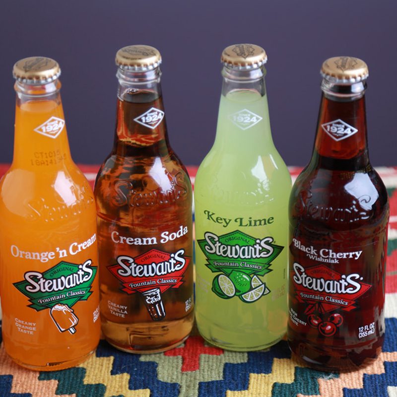 A bottle of Stewart's Orange 'n Cream, Stewart's Cream Soda, Stewart's Key Lime, and Stewart's Black Cherry on a table cloth.