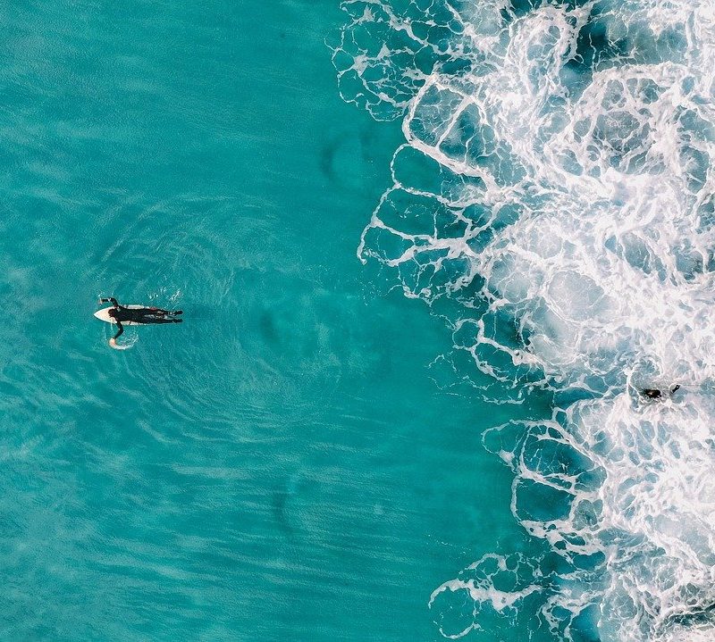 surfer laying on surfboard and paddling in the water.