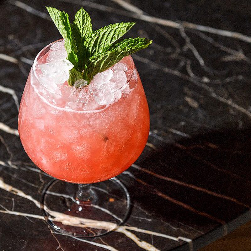 A glass of watermelon cooler with herb on a table.