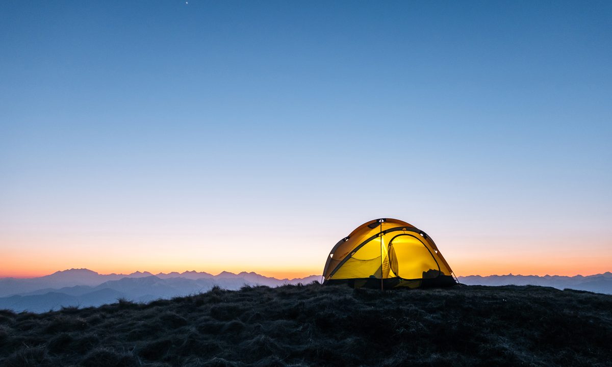 A yellow tent on a mountain ridge at dawn.