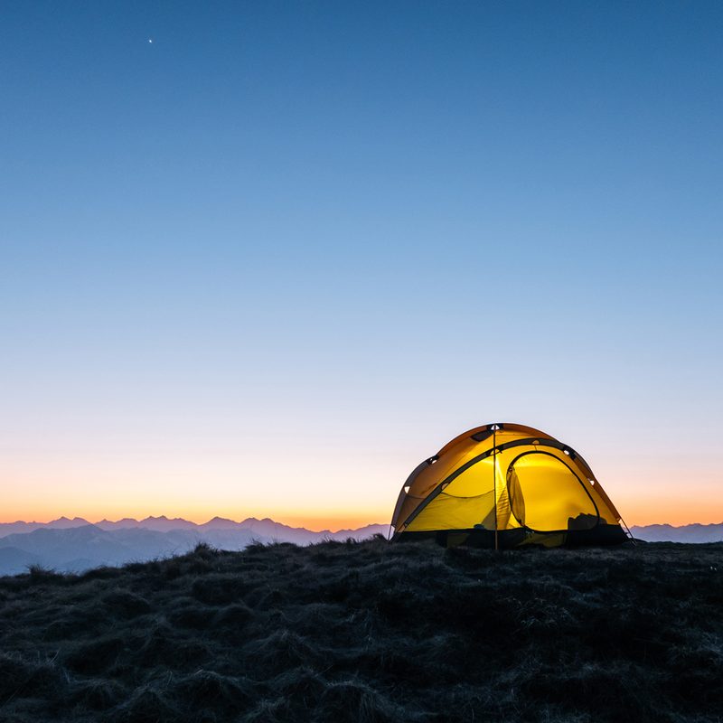 A yellow tent on a mountain ridge at dawn.