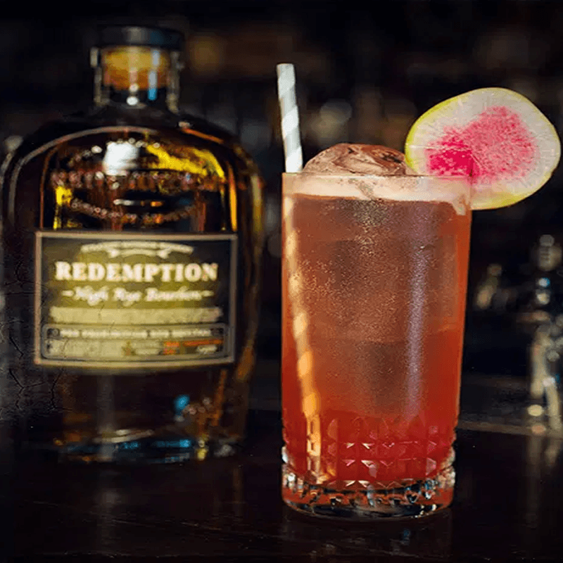 A glass of Watermelon, Sugar, Rye beside a bottle of Redemption High Rye Bourbon.