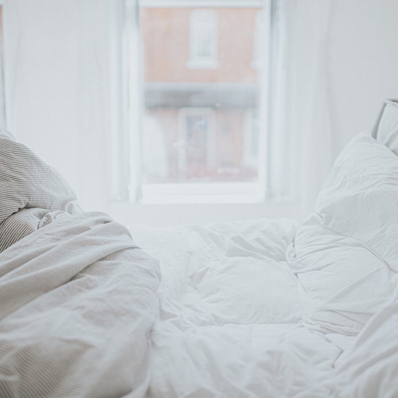 Unmade bed with white blankets and pillows.