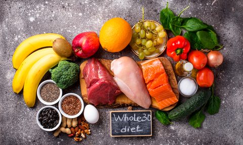 An overhead shot of fruits, vegetables, unprocessed meat, nuts, and seeds with "Whole 30 diet" written on a small blackboard.