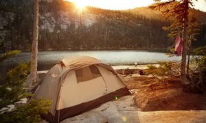 A tent near a body of water with a view of the rising sun.