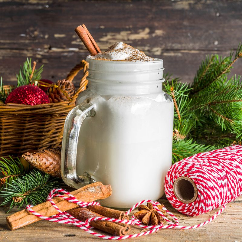 Christmas Tom and Jerry cocktail, whipped cream eggnog with spices, dairy milk beverage, with christmas decorations, rustic wooden background copy space.