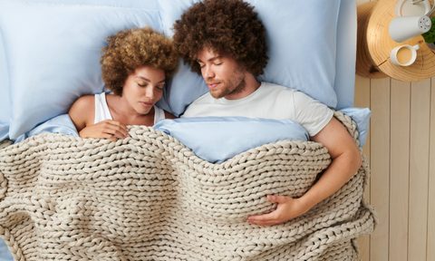 A couple snuggles under Bearaby's weighted, fall-colored blanket