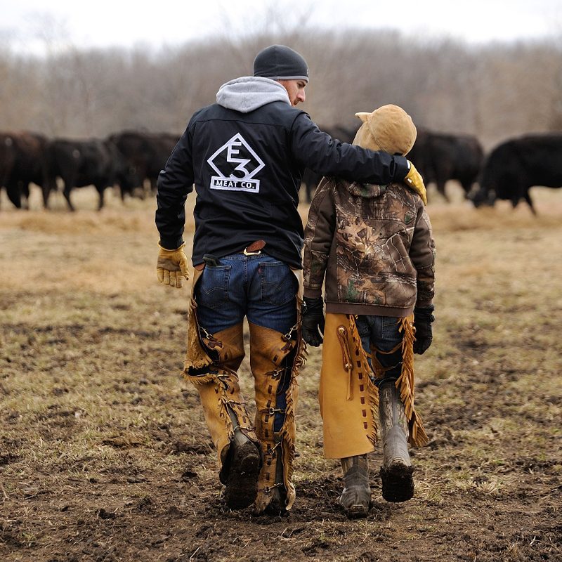 Adam of E3 Ranch with son Drake walking towards cattle.