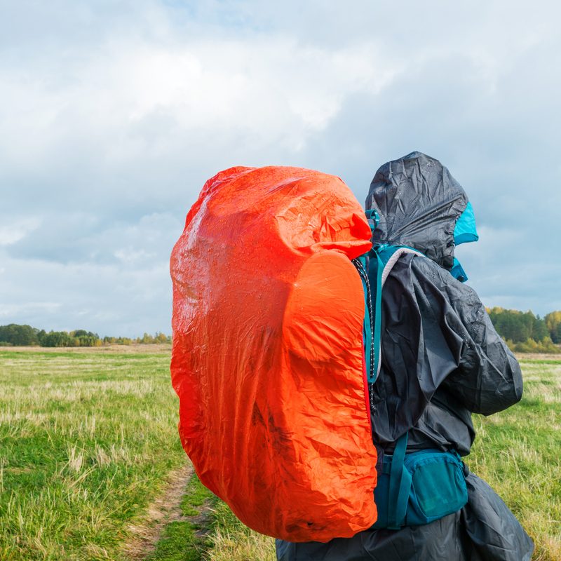 Man hiking with bright red backpack on a green field.